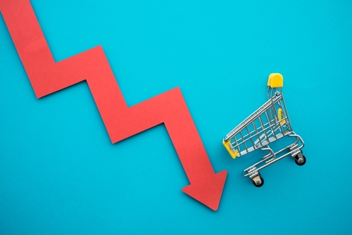 Shopping trolley with red chart falling down on blue background copy space. Global economic recession crisis, core retail sales decrease, inflation or goods price up concept.